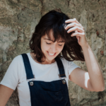 La dramaturga Clàudia Cedó somrient vestida amb una samarreta blanca i un mono de tirants blau (Escenaris Especials/Wikimedia Commons)