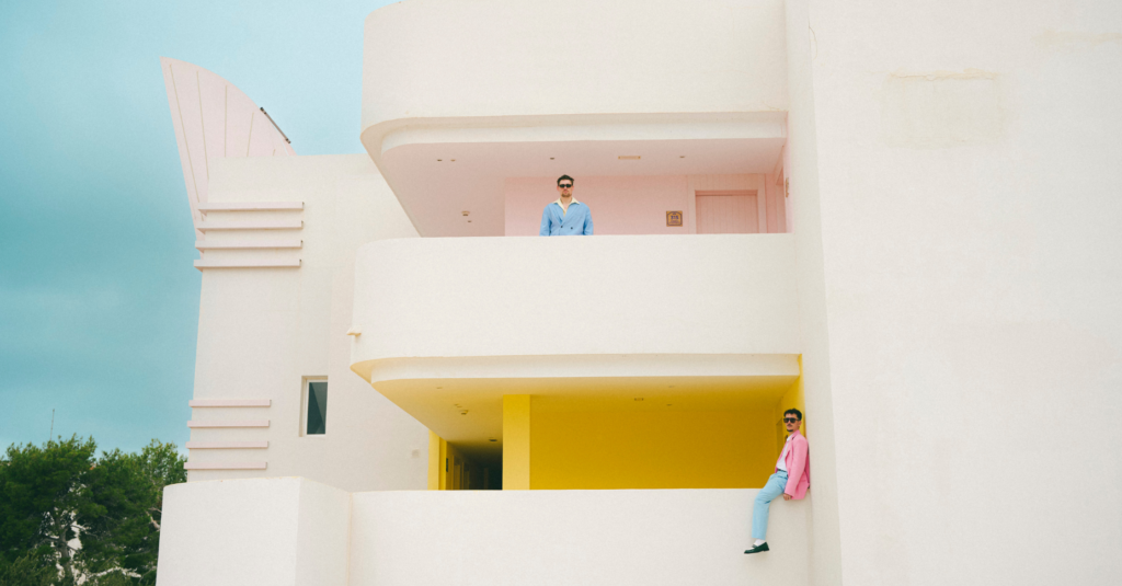 Xavier Coca i Oriol de Ramon vestits amb tons blaus i roses en un balcó d'un edifici