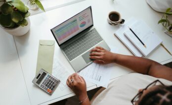 Dona treballant amb un portàtil, una calculadora i un cafè a la taula d'una oficina.